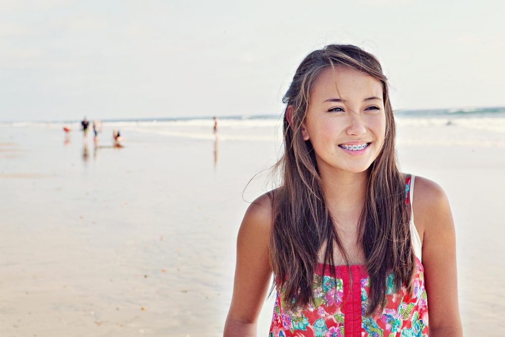 Smiling teenage girl with metal braces standing on the beach, Hulse Orthodontics, Carlsbad CA