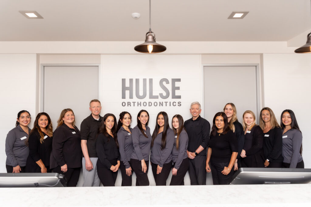 The Hulse Orthodontics team standing behind the reception desk under the Hulse Orthodontics sign, Hulse Orthodontics, Carlsbad CA