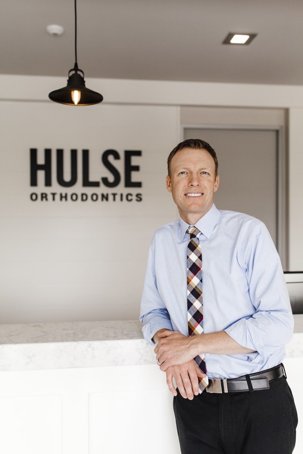 Dr. Cameron Hulse, specialist orthodontist, leaning on the front desk in front of the Hulse Orthodontics sign, Hulse Orthodontics, Carlsbad CA